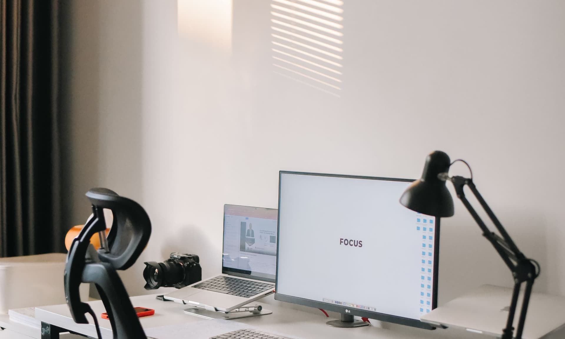 A clean modern office desk with a monitor, laptop and desk lamp